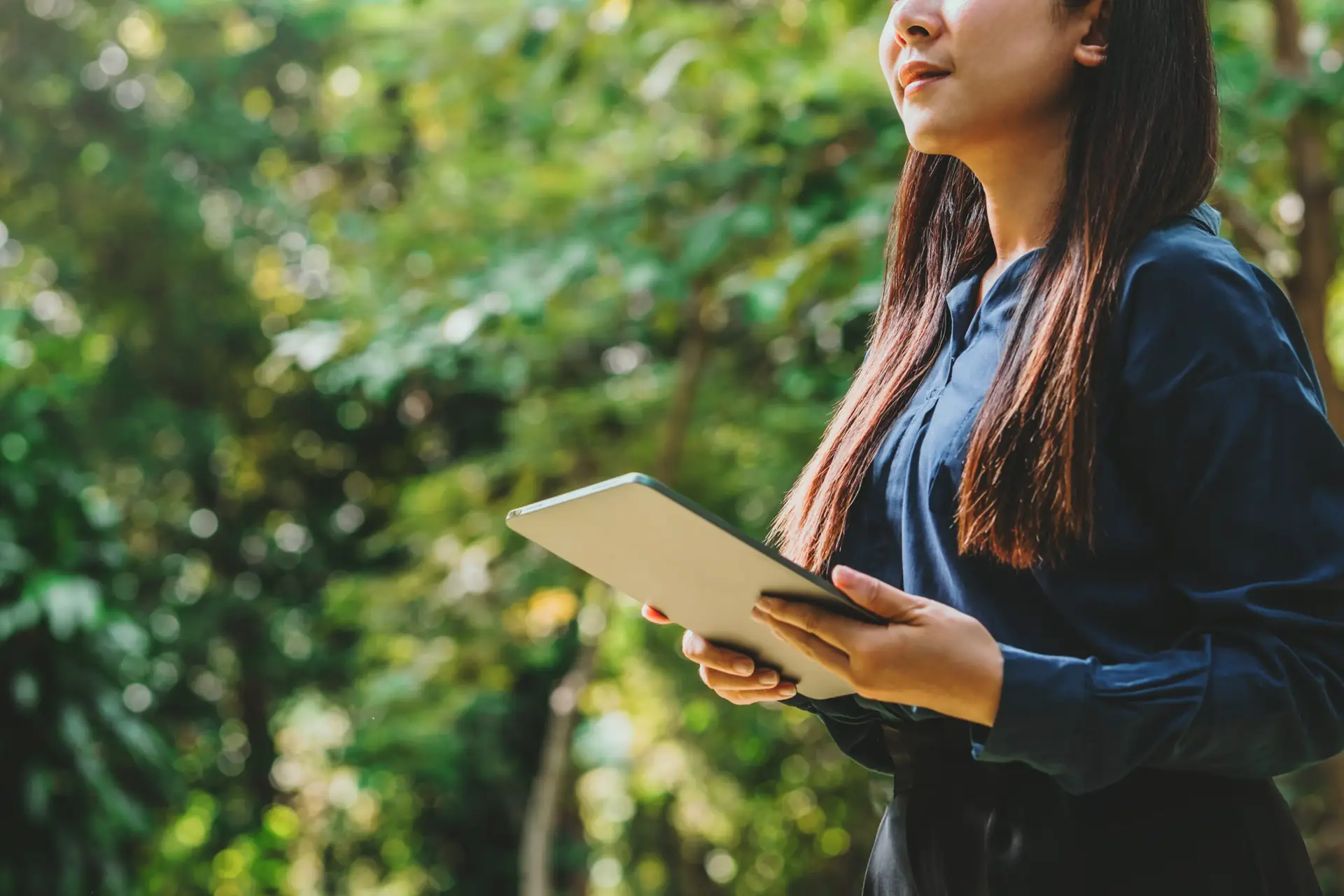 Asian woman holding tablet and smiling with a green backdrop to represent the consumer base waiting to see energy efficiency rolled out through all parts of the supply chain.